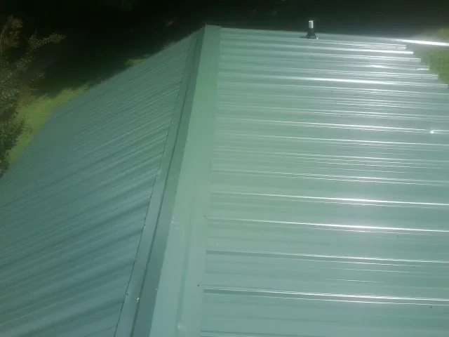 New green metal panels meeting at the ridge of a roof — Flat Roof Repair work by our crew in Hoffman Estates