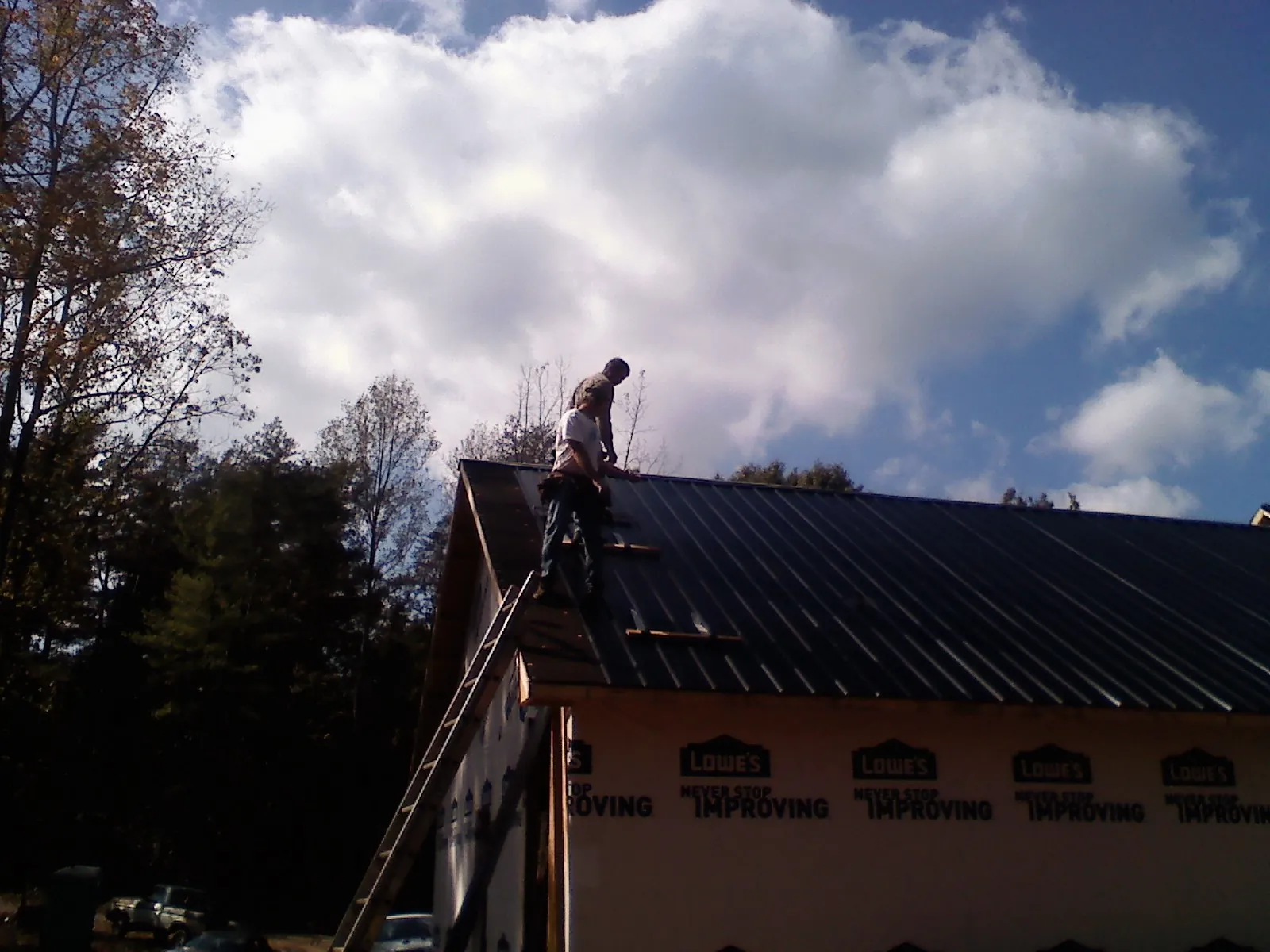 Roofer fastening dark metal panels high against a cloudy sky, from a Roof Inspection job in Hoffman Estates