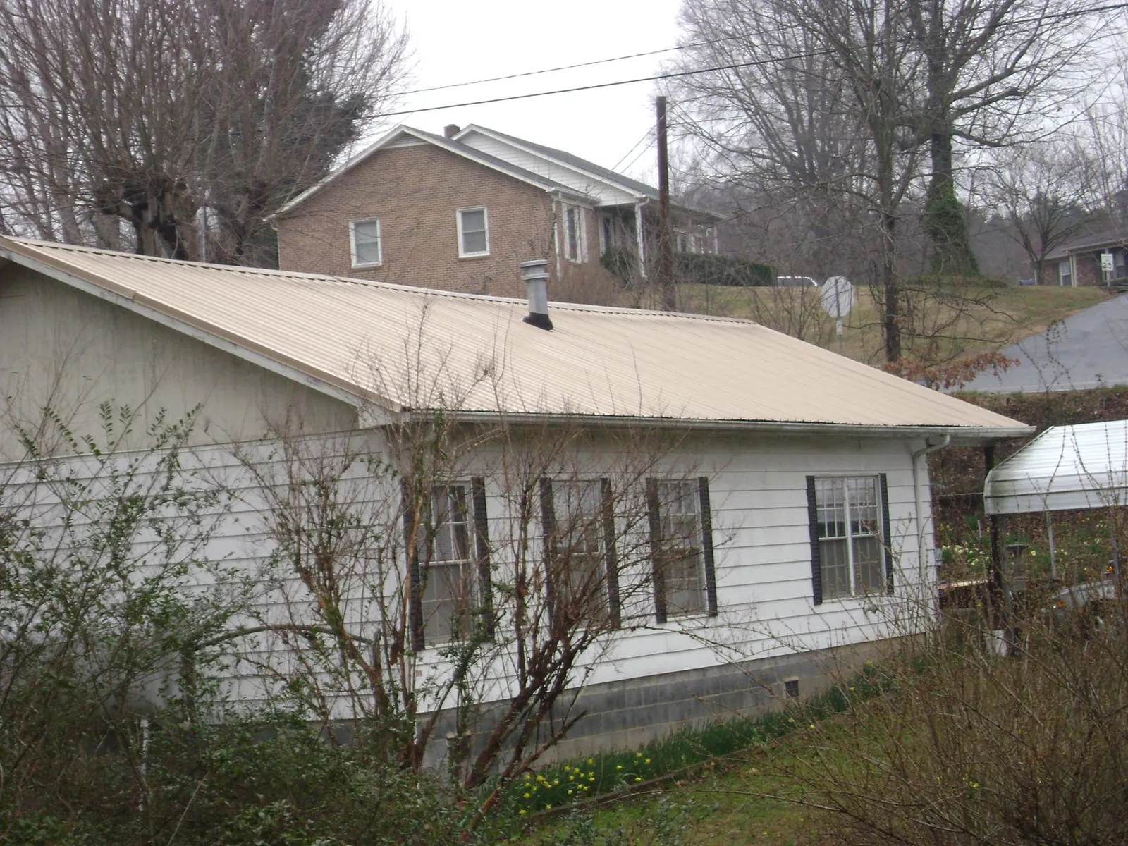 Tan metal roof on a white sided house set into a hillside — Commercial Roofing by Roofing Brothers in Hoffman Estates